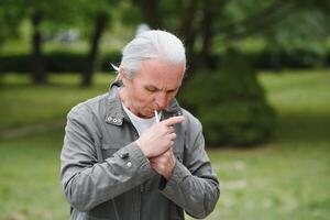 een oud senior Mens roken sigaret buiten, rook verslaving, slecht habbit foto