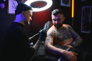 professioneel tatoeëren artiest maakt een tatoeëren Aan een jong Mens hand- foto