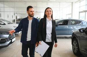 vriendelijk, glimlachen vrouw verkoper tonen merk nieuw auto naar een klant terwijl staand in auto salon foto