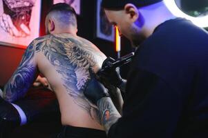 tatoeëren artiest demonstreert de werkwijze van krijgen zwart tatoeëren met verf. meester werken in zwart steriel handschoenen foto
