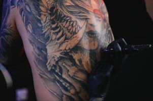 tatoeëren artiest Mens met zwart handschoenen trekt een ridder tatoeëren Aan de jongens terug in de studio. tatoeëren artiest workflow foto