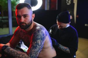 schot van een tatoeëren artiest en een mans terug totaal getatoeëerd met zwart inkt foto