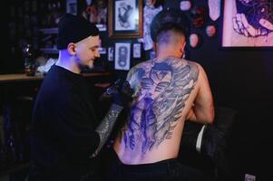 tatoeëren. Mens creëren een afbeelding Aan zijn terug door een professioneel tatoeëren artiest foto