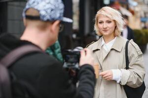 een meisje maakt een blog met een cameraman Aan de straat. jong vrouw blogger, journalist filmen met een professioneel camera en videograaf. foto