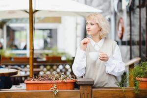 vrolijk elegant jong vrouw in de straat drinken ochtend- koffie in zonneschijn licht. vervelend schattig roze trui, jeans. afgezwakt kleuren foto