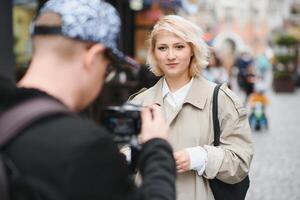 een meisje maakt een blog met een cameraman Aan de straat. jong vrouw blogger, journalist filmen met een professioneel camera en videograaf. foto