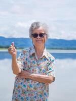 senior vrouw staand en glimlach Bij kant de meer foto