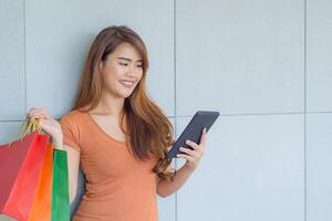 mooi jong vrouw Holding en op zoek Bij tablet met kleurrijk boodschappen doen Tassen. concept van bedrijf en e-commerce foto