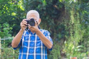 senior Mens het schieten foto door een digitaal camera in de tuin. een ouderen Mens draagt een blauw shirt, gelukkig wanneer gebruik makend van een camera. concept van oud mensen en fotografie