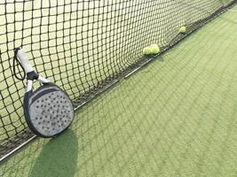 detailopname visie van een peddelen racket en ballen in een padel tennis rechtbank in de buurt de netto. groen achtergrond met wit lijnen. sport, Gezondheid, jeugd en vrije tijd concept. sportief apparatuur. wit lijnen in achtergrond foto