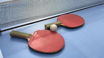 twee tafel tennis rackets en ballen Aan een blauw tafel met netto. foto