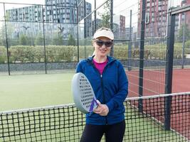 portret van positief jong vrouw met racket en padel bal Aan tennis rechtbank foto