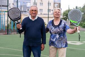 portret van sportief fit senior vrouw spelen padel Aan Open rechtbank Aan zomer dag, klaar naar raken bal. Gezondheid en actief levensstijl concept.. foto