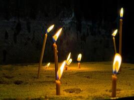 lit kaarsen in zand gevulde kaars houder in kerk tegen donker muur. religieus of geestelijk ceremonie met flikkeren vlammen en warm kaarslicht. brandend kaarsen in kerk. foto