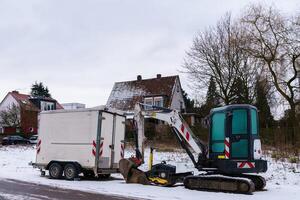 een klein graafmachine en een auto aanhangwagen Aan een met sneeuw bedekt bouw plaats. foto