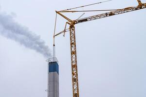 een roken schoorsteen en een bouw kraan tegen een lucht. foto
