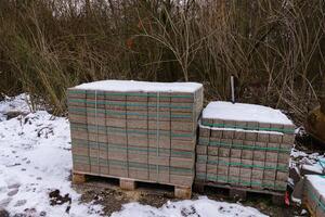 2 houten pallets met weg tegels Aan een met sneeuw bedekt bouw plaats. foto