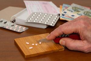 menselijk hand- verdeelt medisch pillen met een mes Aan een houten tafel. dichtbij omhoog. foto
