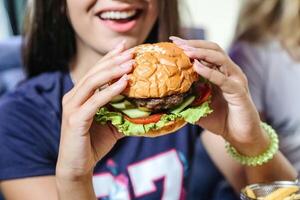 vrouw Holding een Hamburger in voorkant van haar gezicht foto