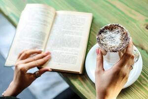 persoon lezing boek en Holding gebakje Bij buitenshuis cafe foto