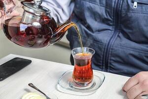 persoon gieten thee in glas kop foto