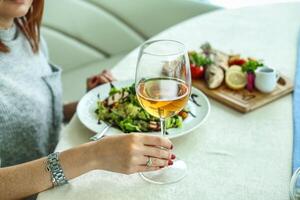 vrouw zittend Bij tafel met bord van voedsel en glas van wijn foto