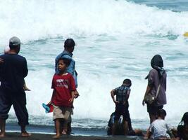 kebumen, centraal Java, Indonesië april 14, 2024 mensen genieten vakantie gedurende helder daglicht Bij ambal strand. zomer familie toerist plek met oceaan Golf achtergrond. foto