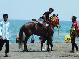 kebumen, centraal Java, Indonesië april 11, 2024 mensen genieten vakantie rijden een paard gedurende helder daglicht Bij ambal strand. zomer familie toerist plek met oceaan Golf achtergrond. foto