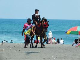 kebumen, centraal Java, Indonesië april 11, 2024 mensen genieten vakantie rijden een paard gedurende helder daglicht Bij ambal strand. zomer familie toerist plek met oceaan Golf achtergrond. foto