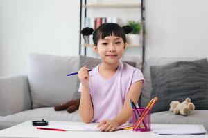 een jong meisje is zittend Bij een tafel met een potlood en een kop van kleurpotloden foto
