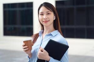 een bedrijf vrouw vervelend een blauw overhemd en Holding een kop van koffie en een tablet foto