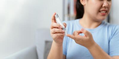 Aziatisch vrouw gebruik makend van lancet Aan vinger voor controle bloed suiker niveau door glucose meter foto