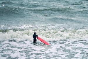 mannelijke surfer in zwempak in zeegolven met rode surfplank foto