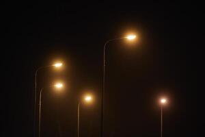 nacht lantarenpaal schijnt met flauw mysterieus geel licht door avond mist Bij stil stad nacht foto