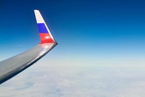 vliegtuig vleugel met Russisch vlag kleuren over- wolken antenne visie van vliegtuig venster, onderdelen probleem foto