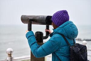 vrouw op zoek door verrekijker kijker Bij zee in winter foto