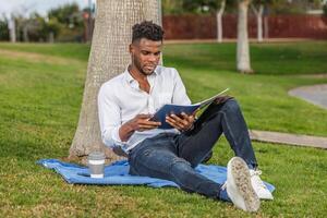 Mens ontspannende en lezing een boek in de schaduw van een boom foto