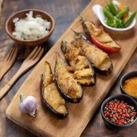 vis bakken gebakken aubergines ui paprika's Aan hout bord specerijen in klein kommen foto