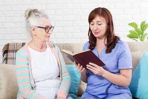 vrouw leest een boek aan een bejaarde vrouw in verpleeghuis foto