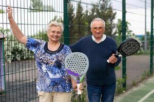 portret van sportief fit senior vrouw spelen padel Aan Open rechtbank Aan zomer dag, klaar naar raken bal. Gezondheid en actief levensstijl concept.. foto