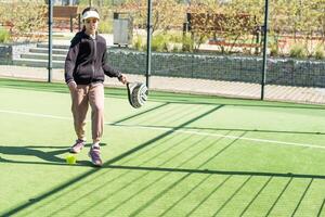 weinig meisje spelen padel en raken de bal met zijn racket buitenshuis sport- concepten foto