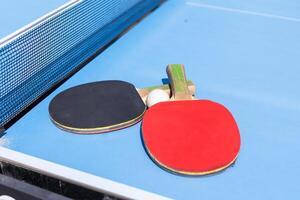 twee tafel tennis of ping pong rackets en bal Aan blauw tafel met netto foto