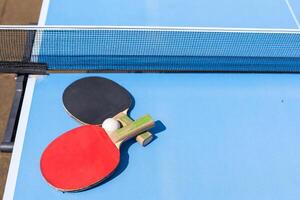 twee tafel tennis of ping pong rackets en bal Aan blauw tafel met netto foto