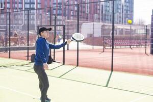 een vrouw met racket en bal achter de netto in peddelen tennis rechtbank klaar voor opleiding foto