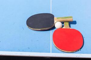 rood en zwart tafel tennis peddels en bal Aan de blauw tafel tennis tafel met netto. ping pong concept met kopiëren ruimte foto