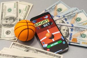 smartphone met het gokken mobiel toepassing en basketbal bal met geld detailopname. sport en wedden concept foto