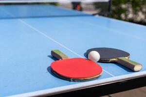 rood en zwart tafel tennis peddels en bal Aan de blauw tafel tennis tafel met netto. ping pong concept met kopiëren ruimte foto