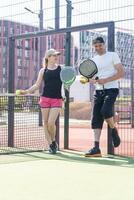 vrolijk atletisch paar lachend gedurende padel tennis bij elkaar passen Aan buitenshuis rechtbank. foto