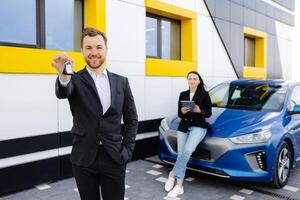 zelfverzekerd mannetje winkel assistent in formeel kleren Holding sleutel en op zoek Bij camera Bij auto- auto handelaar winkel buitenshuis foto