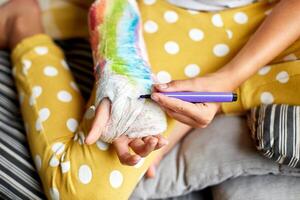 tiener meisje met een gebroken arm Bij huis trekt een orthopedische gips foto